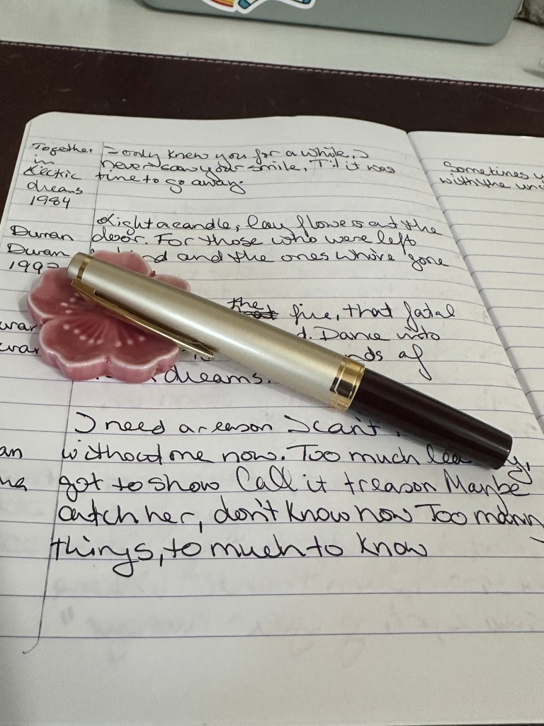 A capped E95S Fountain Pen in Burgandy and Ivory sits on a pink flower pen rest beneath it is a page written in a common book.
